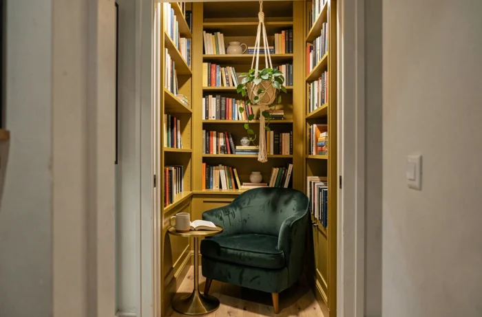 Coin lecture cosy avec fauteuil en velours vert et bibliothèque murale colorée dans un appartement à la décoration intérieure unique et tendance
